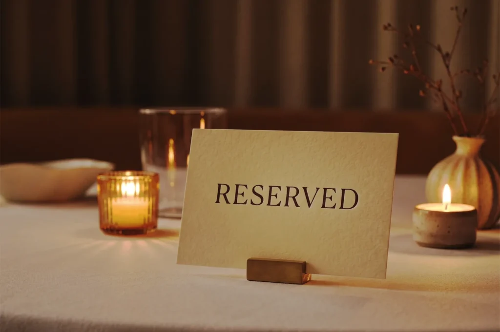 Elegant close‑up of a “Reserved” sign on a softly lit table with candles, glassware, and minimalist decor, evoking a warm and intimate dining atmosphere ideal for romantic or private occasions.
