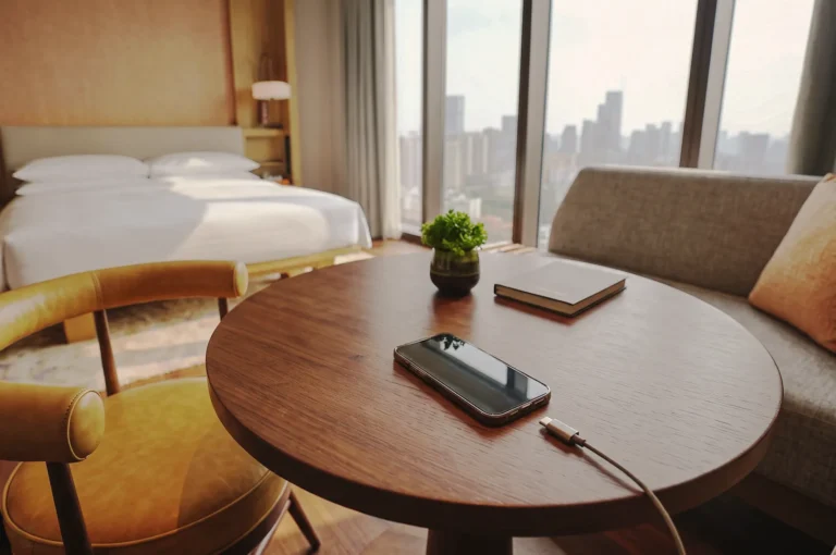 Smartphone charging on a round wooden table in a luxury hotel room with city skyline views.