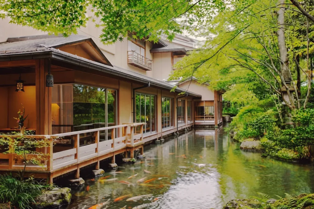 Japanese ryokan with wooden walkway above a koi pond surrounded by green maple trees, reflecting tranquil traditional Japanese garden design.