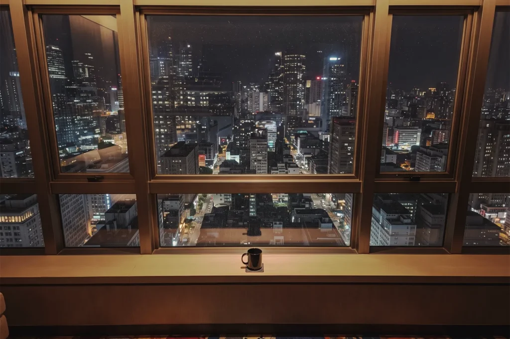 Single dark coffee mug resting on a wide windowsill overlooking a sprawling, illuminated city skyline at night.