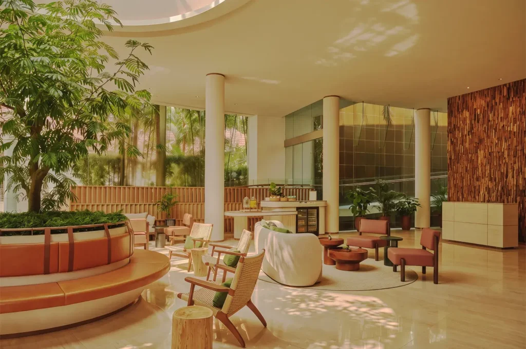 Contemporary hotel lobby with natural light, indoor greenery, and minimalist furniture in warm earthy tones — modern tropical interior design in Singapore resort.