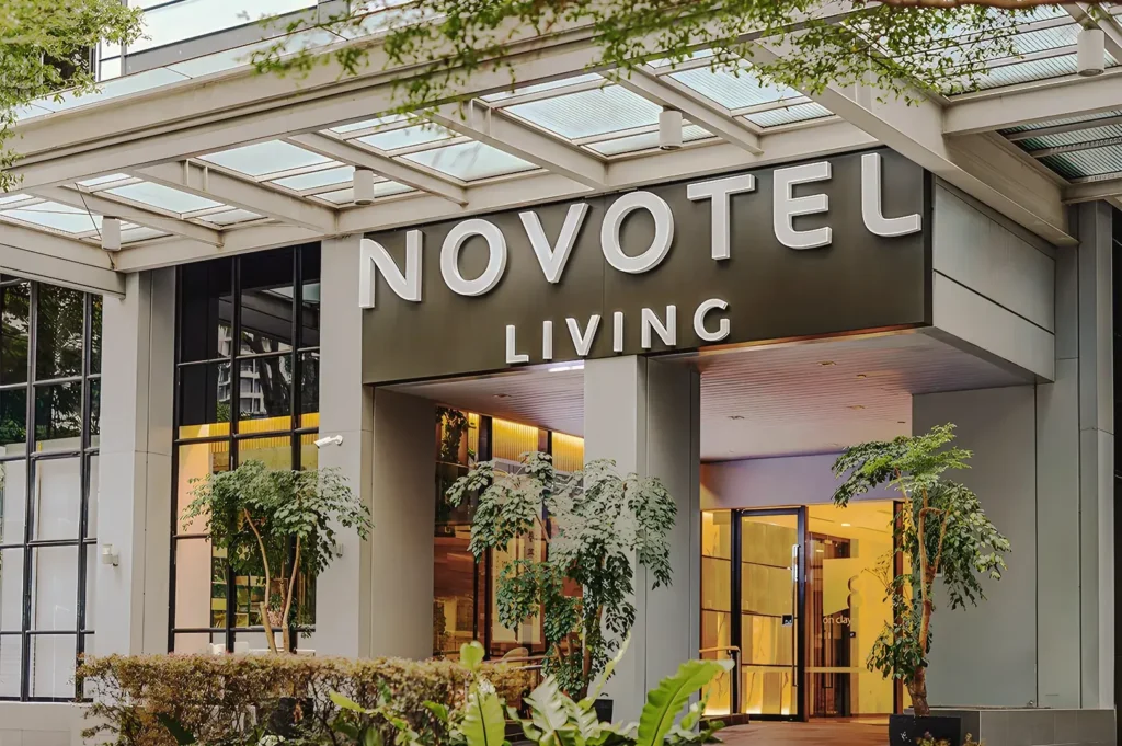 Main entrance of Novotel Living Singapore with glass façade, greenery, and modern design welcoming guests to upscale serviced apartments.