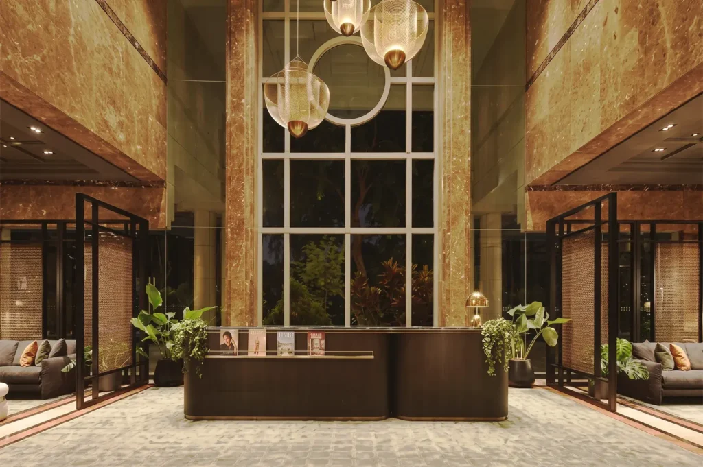 Luxurious marble‑clad lobby of Adina Serviced Apartments Singapore Orchard with stylish pendant lights, greenery, and a sophisticated reception desk.