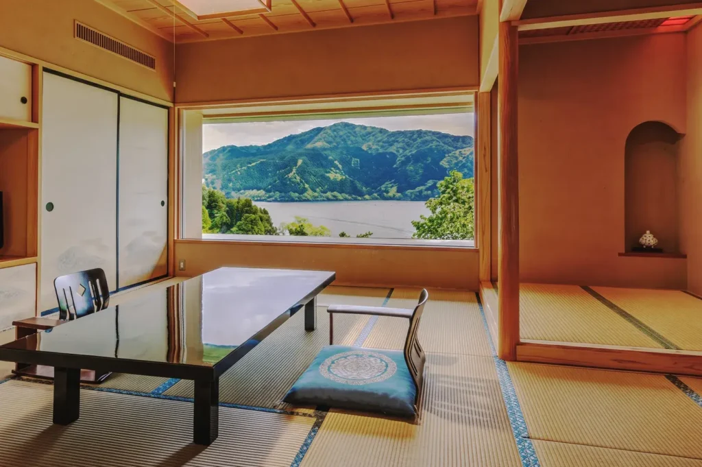 Japanese tatami room with low table and floor chairs overlooking scenic mountains and a lake, showcasing minimalist ryokan interior design.