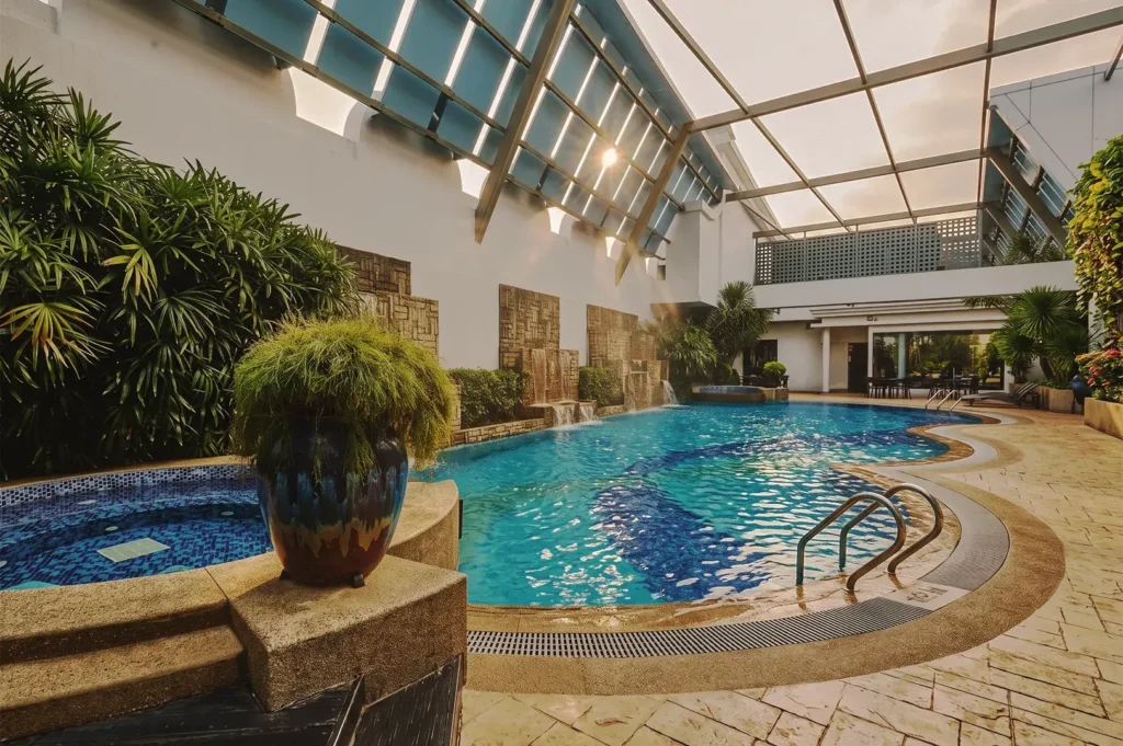 Inviting indoor swimming pool at Adina Serviced Apartments Singapore Orchard with cascading water features, tropical plants, and natural sunlight.