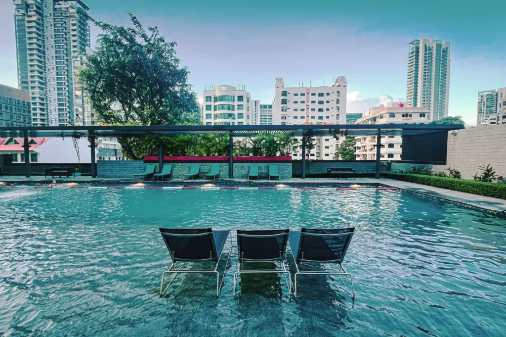 Aloft Singapore swimming pool with submerged lounge chairs and city skyline backdrop — relaxing outdoor leisure space in modern hotel setting.