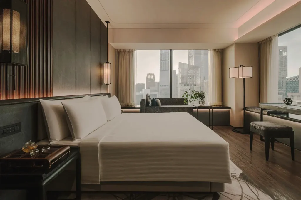 Luxurious hotel room in Singapore with a king‑size bed, modern decor, and panoramic city views through large windows — representing comfort, style, and premium accommodation.