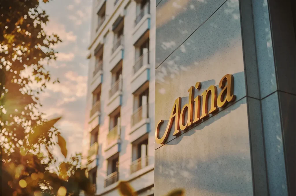Golden Adina logo on the building facade at Singapore Orchard, captured during sunset with soft light and urban architectural details.