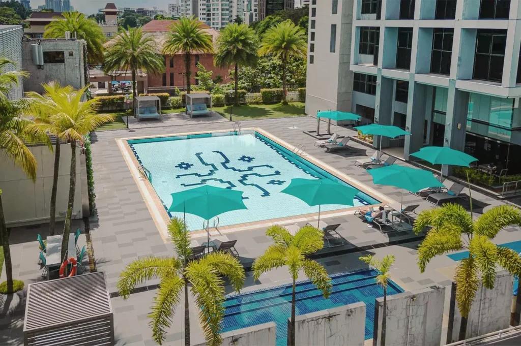 Outdoor swimming pool at Novotel Living Singapore with turquoise umbrellas, palm trees, and modern leisure facilities.