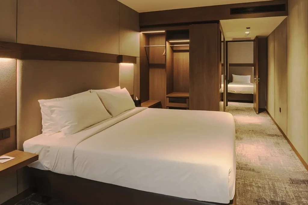 Contemporary hotel room at 30 Bencoolen Singapore with king‑size bed, warm lighting, minimalist wooden furniture, and connecting bedroom for comfortable city accommodation.