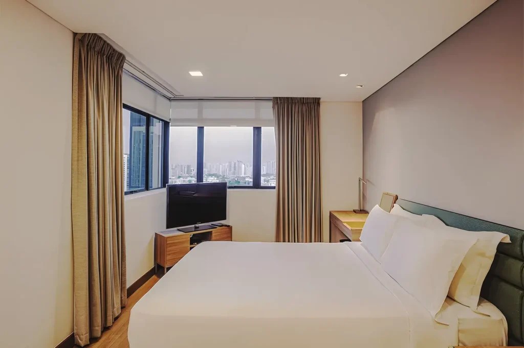 Modern bedroom at Novotel Living Singapore with city view, minimalist décor, large windows, and comfortable queen bed.