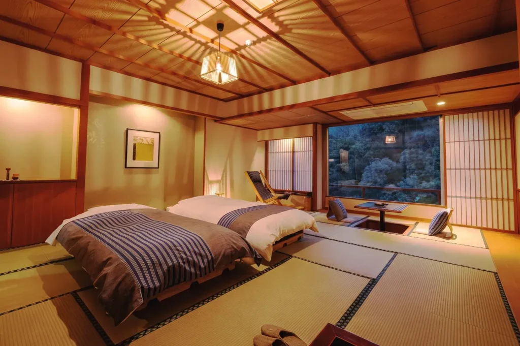 Elegant Japanese ryokan bedroom with tatami flooring, twin beds, shoji screens, and panoramic forest views, blending comfort and traditional design.