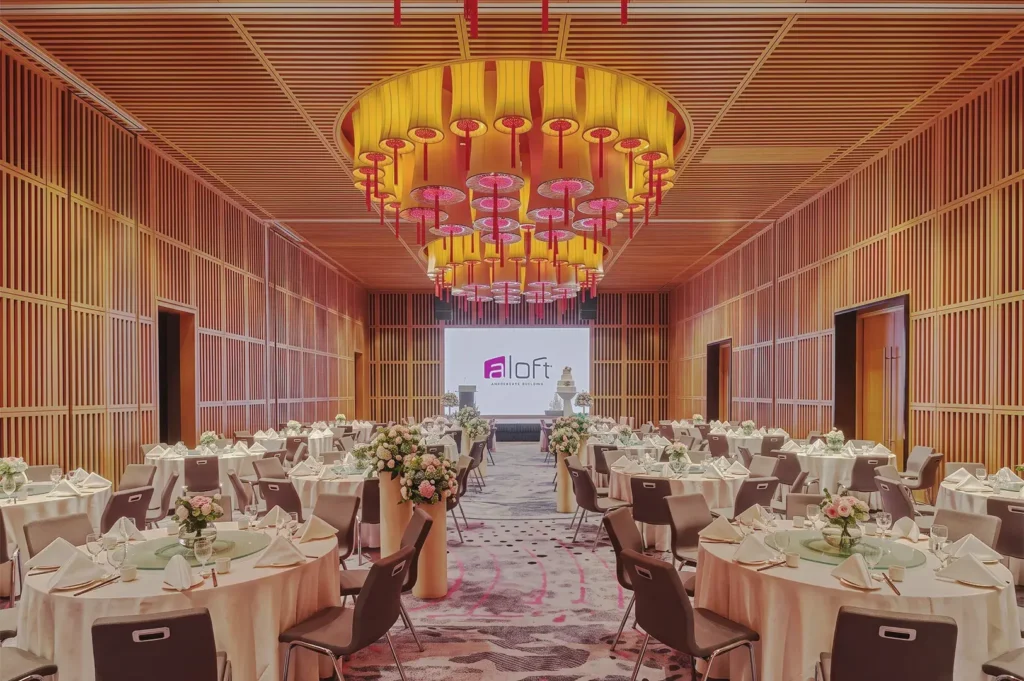 Elegant Aloft Singapore ballroom with round tables, floral centerpieces, and lantern‑style ceiling lights — modern venue for weddings and corporate events.